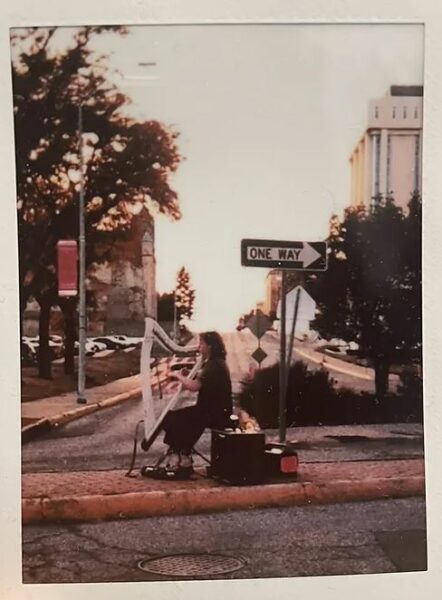 Gallery 2 - A solo female harpist plays underneath a street sign that says \\\